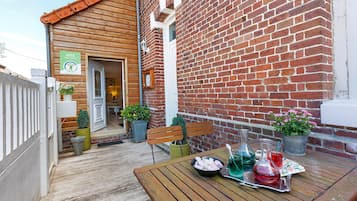 A wooden deck with a table set for dining, a brick wall, and a door leading to a room.