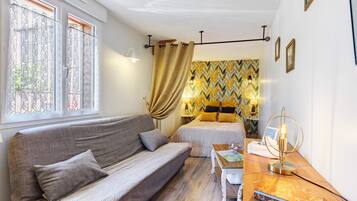 Een gezellige kamer met een bank, een bed met gordijnen met een patroon, en een nachtkastje met een lamp.