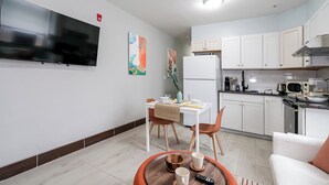 A modern kitchen with white cabinets, a refrigerator, and a microwave. There is a dining area with a table and chairs, and a flat-screen TV mounted on the wall. - Lancaster Art Suite 4 - 2BR near Drexel & Penn (Philadelphia)