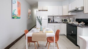 A modern kitchen with white cabinets, a black stove, and a dining area with a table set for two. - Lancaster Art Suite 4 - 2BR near Drexel & Penn (Philadelphia)