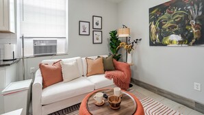 A modern living room with a white sofa, a round coffee table, and a large painting on the wall. - Lancaster Art Suite 4 - 2BR near Drexel & Penn (Philadelphia)