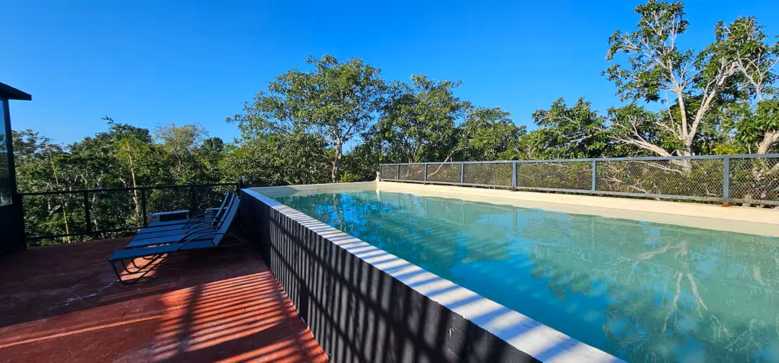 Une piscine avec une rambarde en métal, un banc et un espace ombragé doté d’un sol rouge.