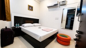 Habitación de hotel con cama, maleta, botella de agua, aire acondicionado, ventana y puerta.