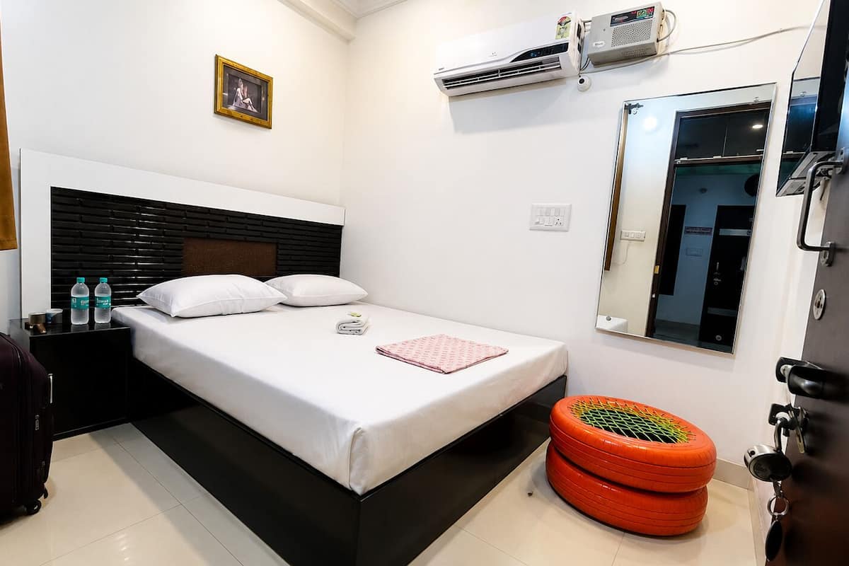 A hotel room with a bed, a suitcase, a water bottle, an air conditioner, a window, and a door.