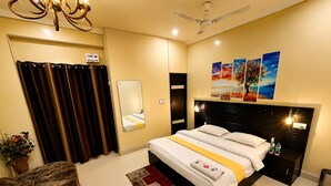 Habitación de hotel con cama, mesita de noche, espejo, ventilador de techo y ventana con cortinas.