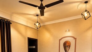 Habitación de hotel con una cama grande, ventilador de techo, mesita de noche con lámpara y un adorno en la pared.