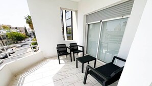 Ein Balkon mit weiß gefliestem Boden, zwei schwarzen Stühlen, einem kleinen Tisch und einem großen Fenster.