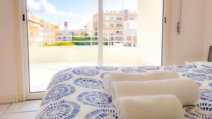 Ein Hotelzimmer mit Bett, Blick auf Gebäude durch eine Glastür und einem weißen Handtuch auf dem Bett.
