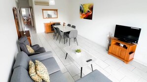 Ein modernes Wohnzimmer mit einer Couch, einem Esstisch, Stühlen, einem Fernseher und einem Couchtisch.