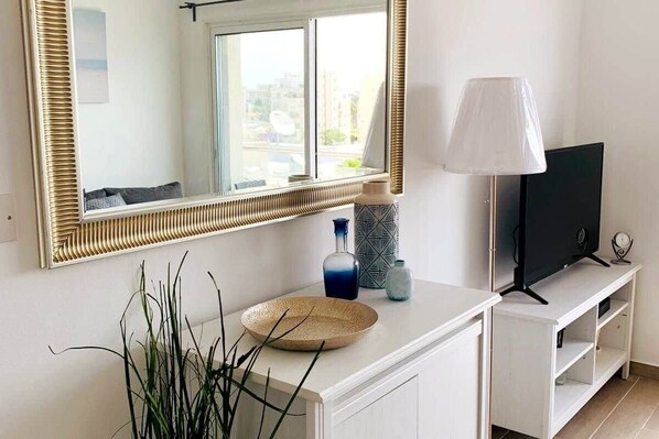 Ein Zimmer mit einem großen Spiegel, einem Fernseher auf einem weißen Schrank, einer Lampe und einer Pflanze.