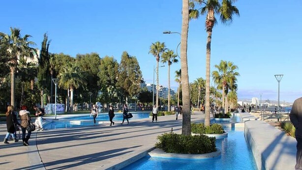 Una plaça pública amb una font al centre, palmeres i persones passejant.