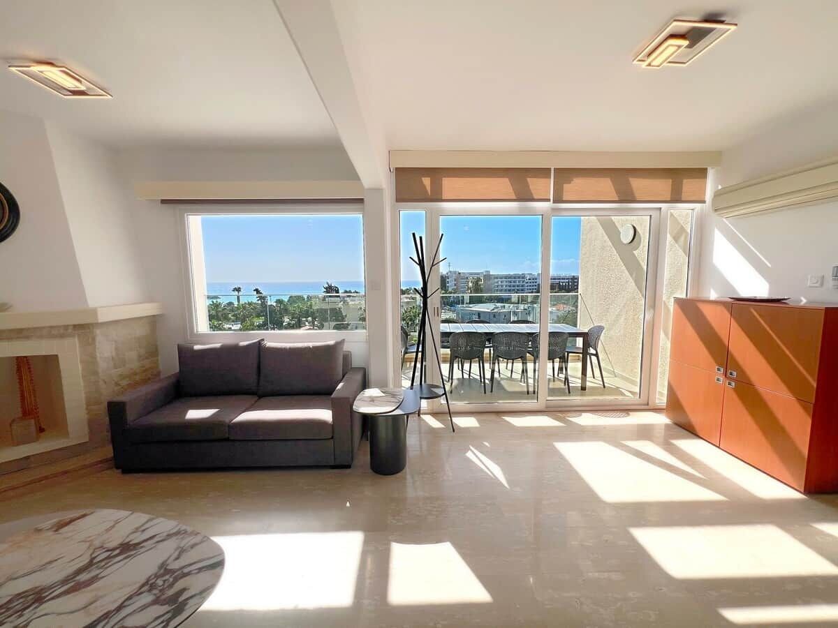 A spacious living area with a sofa, a small table, and a view through large windows.