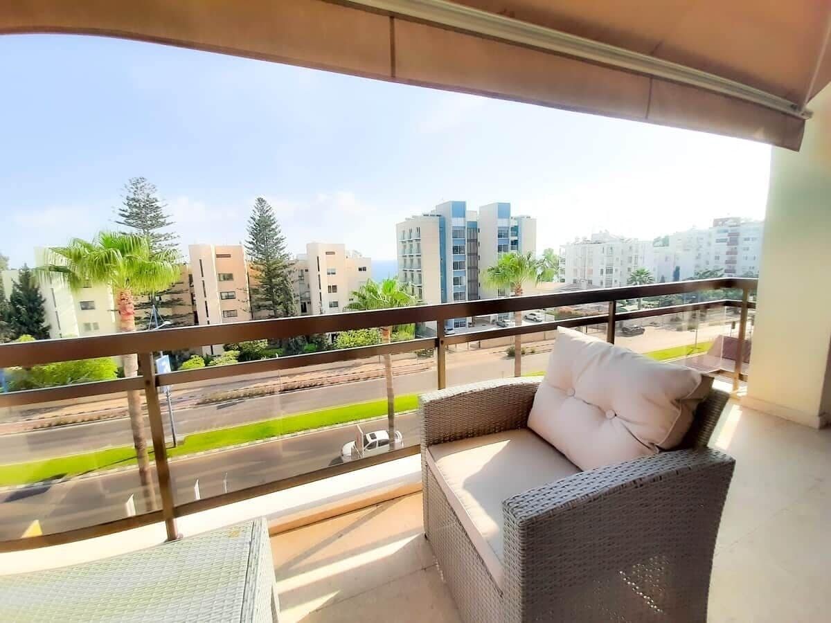 A balcony with wicker furniture, a view of a road, and buildings in the background.