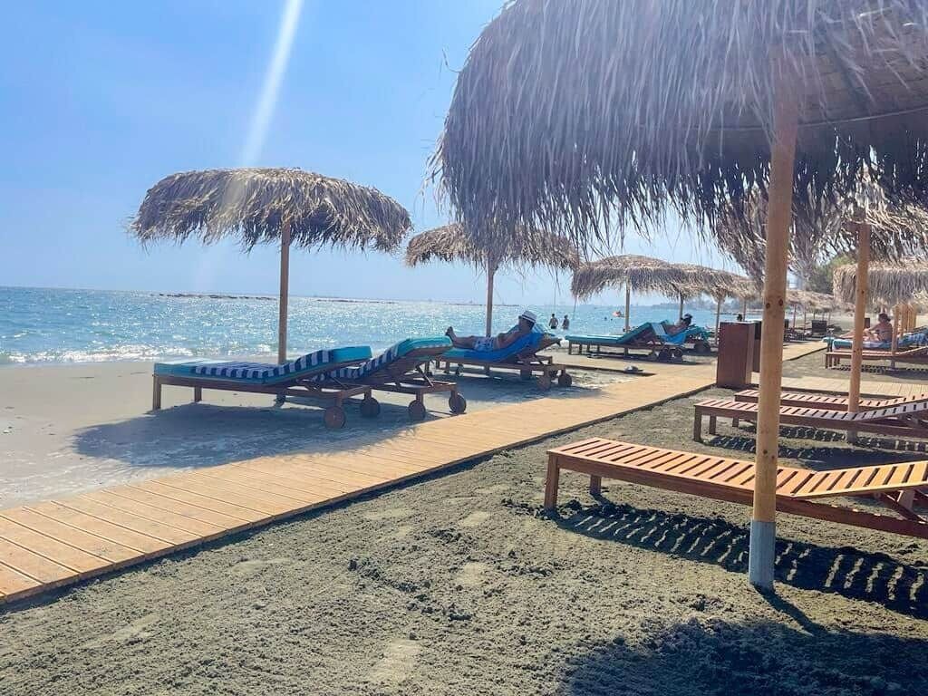 Une plage avec des chaises longues et des parasols en chaume.