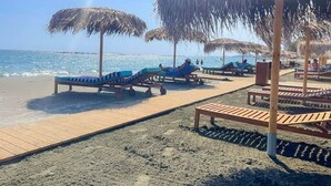 A beach with sun loungers and thatched umbrellas.