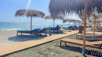A beach with sun loungers and thatched umbrellas.