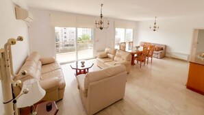 A spacious living room with a sofa set, a dining table with chairs, and a chandelier.