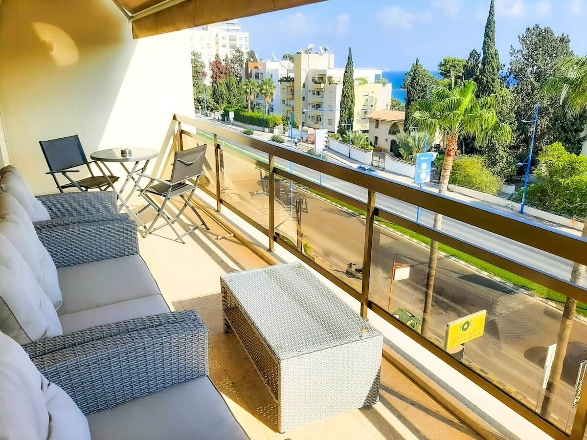 A balcony with wicker furniture, a view of the city, and a clear sky.