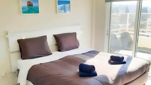 Una habitación de hotel moderna con una cama grande, dos almohadas, una ventana con vistas y dos cuadros enmarcados en la pared.