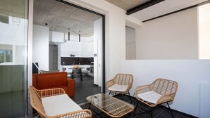 A modern interior with wicker furniture, a glass table, and a view into a kitchen area. - Bridge House 202-2BR Modern Apt. (Limassol)