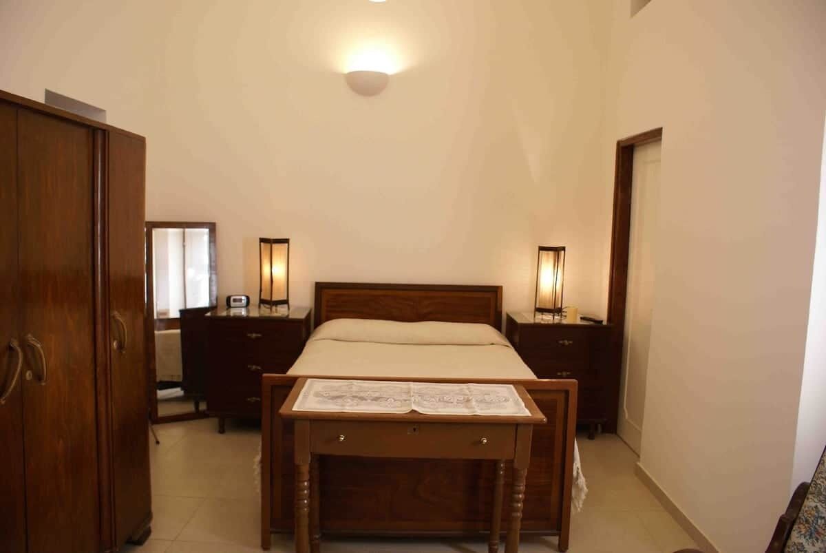 A bedroom with a wooden bed, bedside tables, a wardrobe, and a ceiling light.