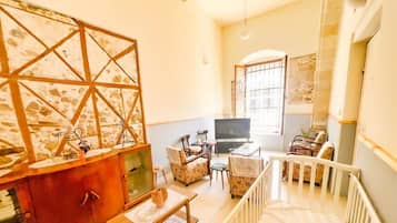 A spacious living area with a high ceiling, a television, and a staircase leading to an upper level.