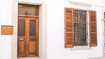 A white building with a wooden door and window with shutters.