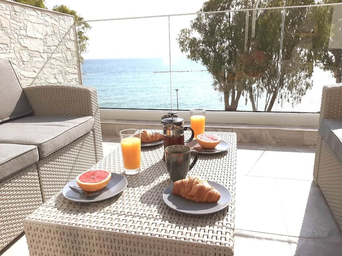 Un desayuno al aire libre con vista al mar, mobiliario de mimbre y una pared de piedra.