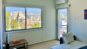 Una habitación con un ventanal grande, una cama, un escritorio y un equipo de aire acondicionado.