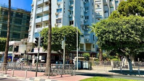 Un edificio residencial de varios pisos con balcones, una calle en primer plano y palmeras.