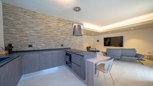 A modern kitchen with a built-in island, a dining area with a table and chairs, and a grey sofa in a living space.