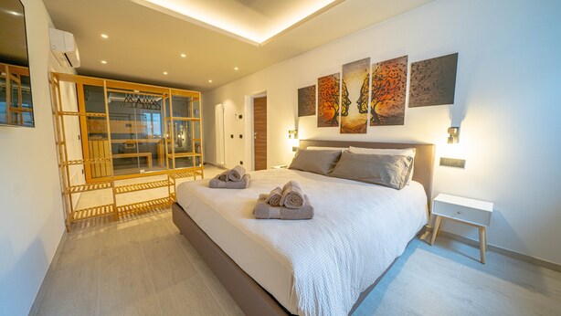 A modern bedroom with a large bed, a wooden wardrobe, and artwork on the wall.