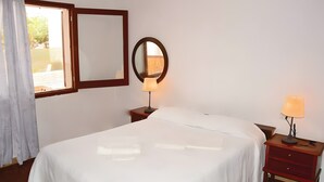 Quarto de hotel com uma cama, uma mesa de cabeceira com luminária, um espelho e uma janela com cortinas.