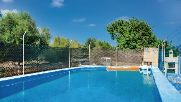 Piscina azul clara com área cercada, rodeada por árvores e um céu limpo.