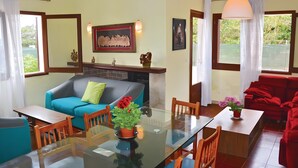 Uma sala de estar com uma mesa de jantar de vidro, sofás azuis e vermelhos, lareira e uma janela grande.