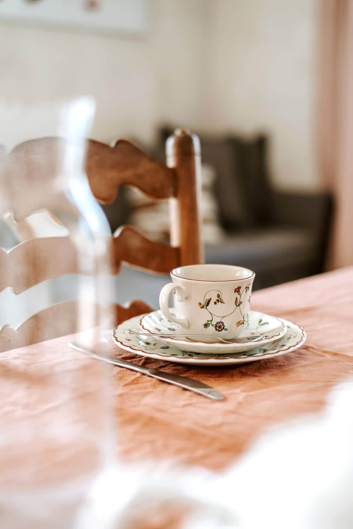 Un tavolo con una tazza e un piattino, un cucchiaino e una sedia.