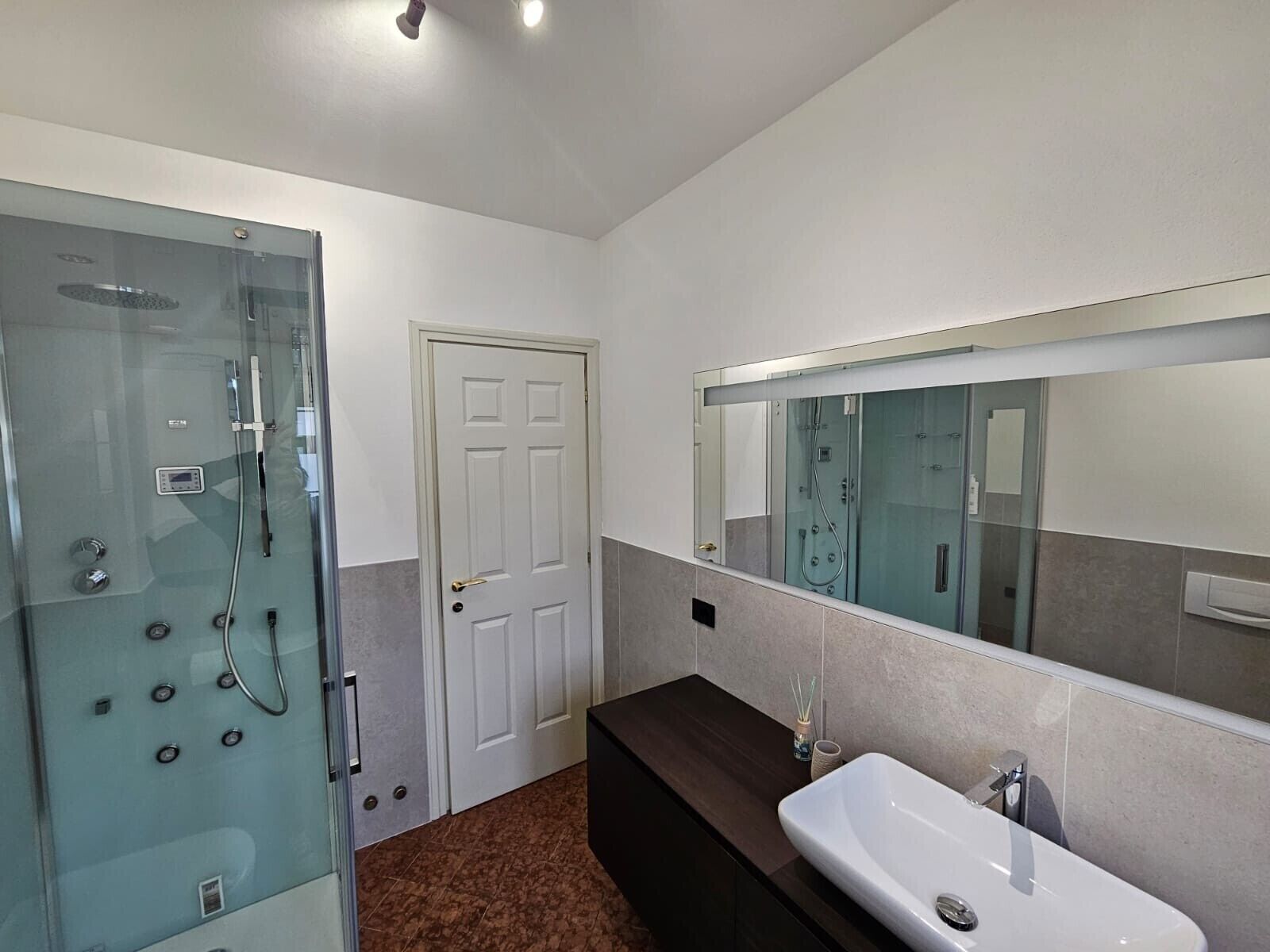 A modern bathroom with a glass-enclosed shower, a white sink, and a large mirror.