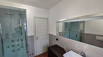 A modern bathroom with a glass-enclosed shower, a white sink, and a large mirror.