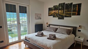 Ein Schlafzimmer mit einem großen Bett, Blick durch eine Schiebetür und drei gerahmte Bilder an der Wand.