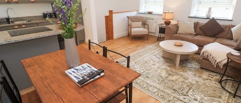 A modern kitchen with a built-in stove, a dining table with chairs, a sofa, a coffee table, and a decorative vase with flowers.