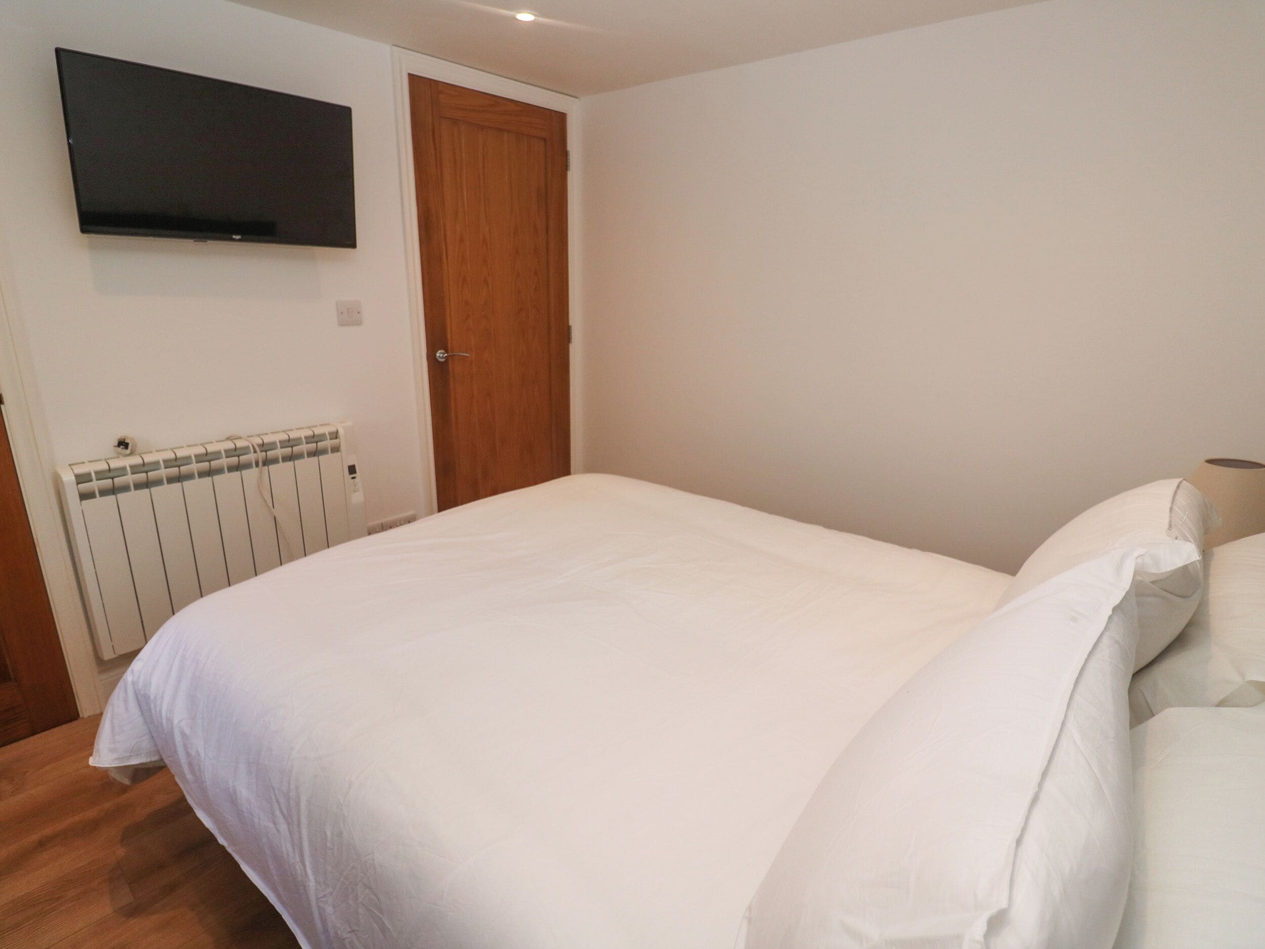 Un dormitorio con cama, puerta de madera, radiador y televisor montado en la pared.
