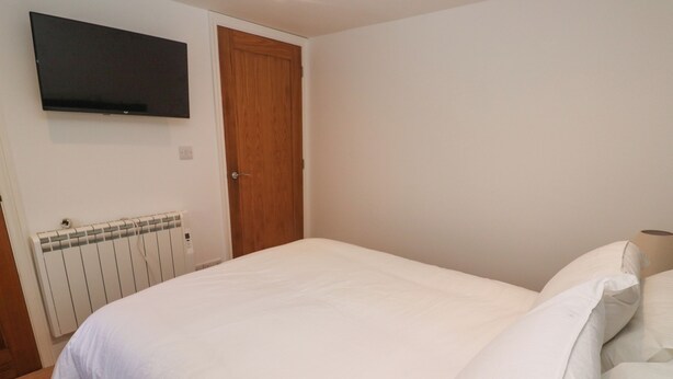 Un dormitorio con cama, puerta de madera, radiador y televisor montado en la pared.