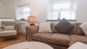Una sala de estar con un sofá marrón, una mesa de centro de madera, un sillón beige y una lámpara.