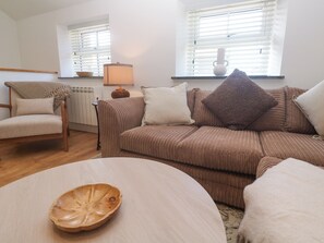 Una sala de estar con un sofá marrón, una mesa de centro de madera, un sillón beige y una lámpara.