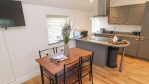 Una cocina moderna con comedor, un televisor montado en la pared y una ventana con persianas.