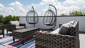 Een terras op het dak met rieten meubilair, waaronder een bank en twee hangstoelen, en een gestreept vloerkleed.