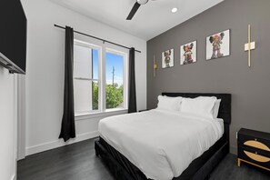 A modern bedroom with a large bed, a window with curtains, and wall art. - Stylish Retreat Near Downtown Houston w/ Rooftop Views (Houston)