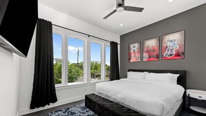 Een slaapkamer met een groot bed, een plafondventilator, een raam met gordijnen en drie ingelijste foto's aan de muur.
