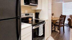 Eine kompakte Küche mit Kühlschrank, Mikrowelle, Herd und Backofen. Es gibt einen Essbereich mit Tisch und Stühlen.