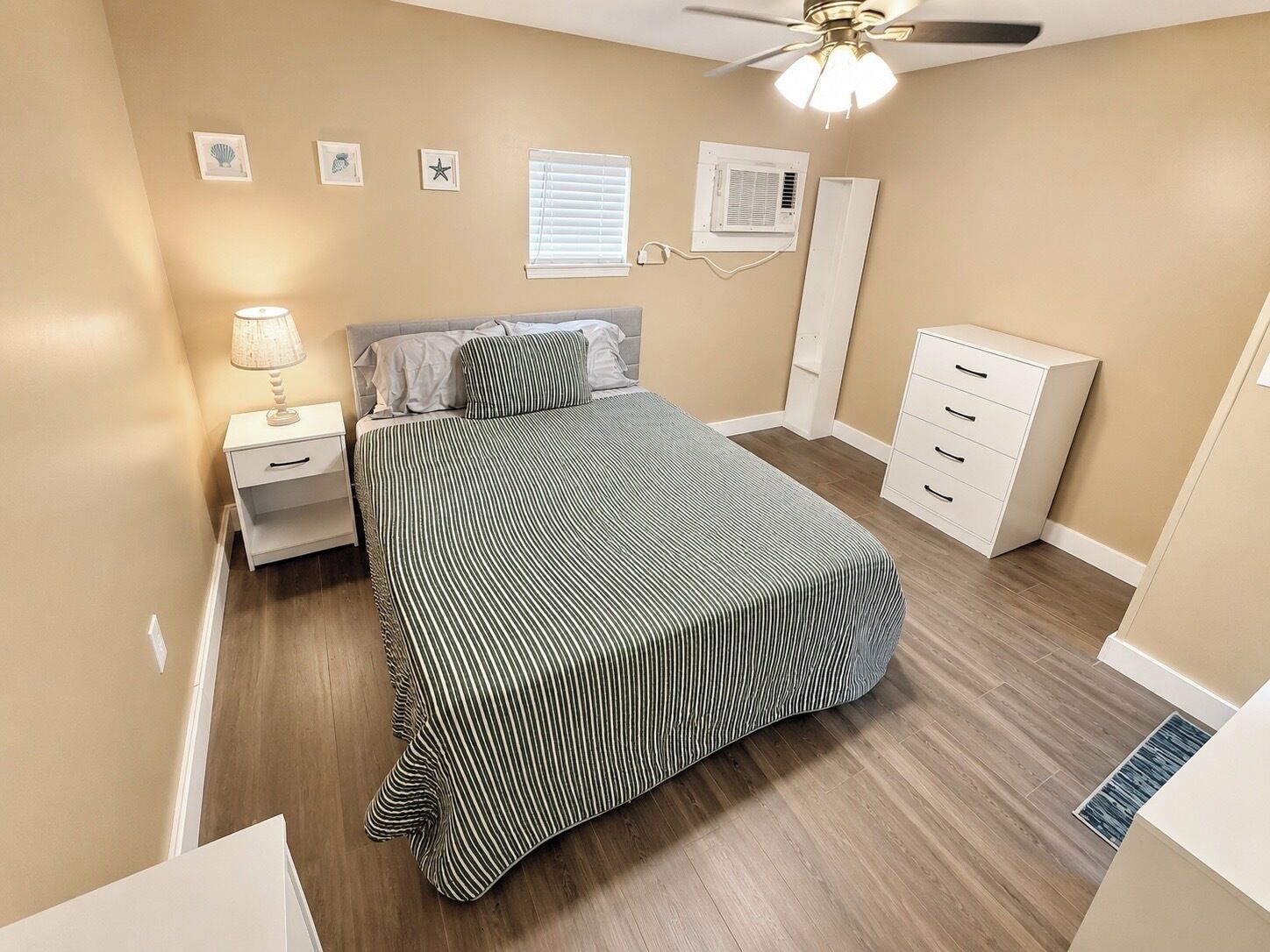 A bedroom with a bed, nightstand, dresser, ceiling fan, and wall-mounted air conditioning unit.